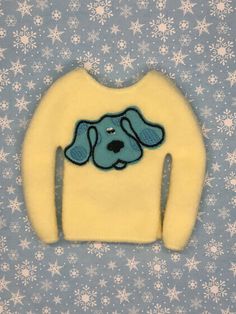 a blue and yellow sweater with a dog's face on it, sitting in front of snowflakes