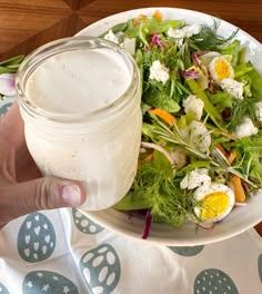 a person holding a mason jar over a salad on a plate with dressing in it