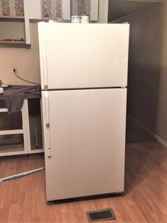 a white refrigerator freezer sitting on top of a hard wood floor in a kitchen