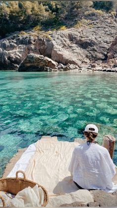 a person sitting on the edge of a cliff overlooking clear blue water and rocky cliffs