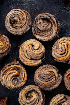 several cinnamon rolls on a black plate with powdered sugar around them and two wooden spoons