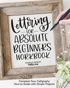 a person holding a pen in front of a wooden frame with the words lettering for absolute beginners workbook