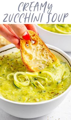 a hand dipping some bread into a bowl of creamy zucchini soup