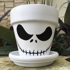 a white planter with a black face painted on the side sitting on a rock