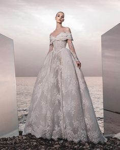 a woman in a wedding dress standing on rocks near the ocean with her hands on her hips