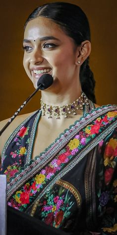 a woman wearing a necklace and holding a pipe in her mouth while standing next to a microphone