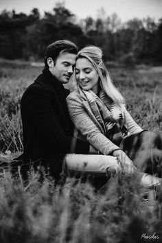 black and white photograph of a couple sitting in the tall grass with their arms around each other