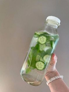 a hand holding a bottle filled with cucumber slices and mint leaves in water