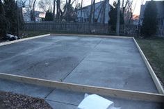 an empty concrete parking lot in the middle of a residential area with trees and houses behind it