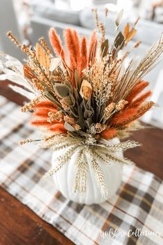 an arrangement of dried flowers in a white pumpkin vase on a plaid tablecloth covered dining room table