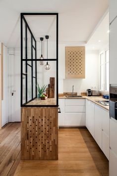 an open kitchen with wooden floors and white cupboards on the walls, along with hanging lights