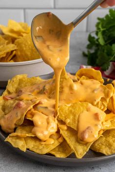 a spoon full of cheese sauce being poured over tortilla chips on a plate