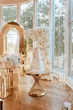 a wedding cake on a table in front of a large window with lots of white flowers