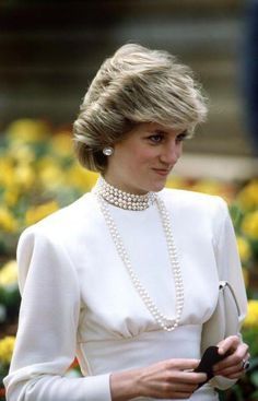 a woman in a white dress with pearls on her neck and necklace, holding a cell phone