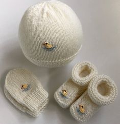 three knitted baby shoes and two hats on a white surface with one ball laying next to it