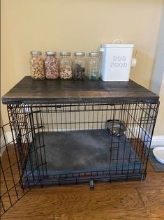 a dog crate with food in it on top of a wooden floor next to a wall