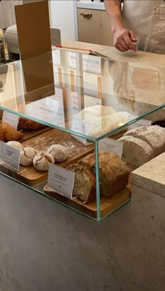 breads and pastries are on display in a glass case at a bakery counter