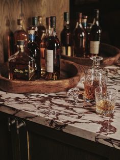 several bottles and glasses on a marble counter top with an old wooden tray in the background