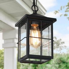 an outdoor light hanging from the side of a house with trees in the back ground