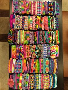 many different colored bracelets are stacked on a black table with a brown chair in the background