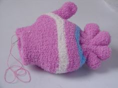 a pink and white knitted fish ornament next to a thread spool