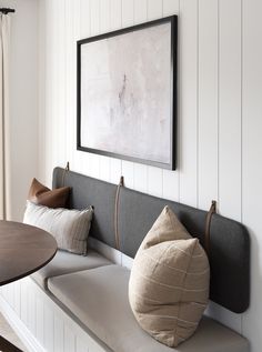 a bench with some pillows on it in front of a wall mounted painting and table