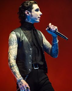 a man with tattoos on his arm holding a microphone and wearing a black leather vest