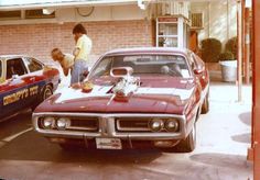 two men working on a car at a gas station with another man standing next to it