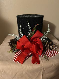 a black top hat with red ribbon and pine cones