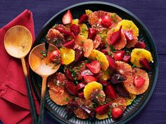 a plate filled with sliced up fruit next to a red napkin and wooden spoons