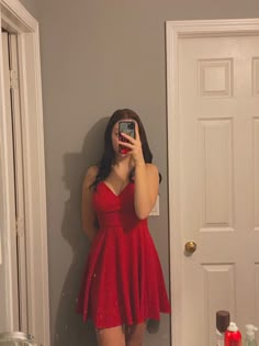 a woman in a red dress taking a selfie with her cell phone while standing next to a door