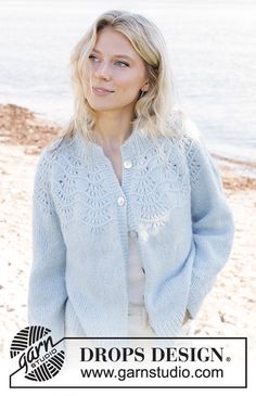 a woman standing on the beach wearing a blue cardigan