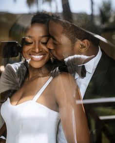 a man and woman standing next to each other in front of a glass window with palm trees behind them