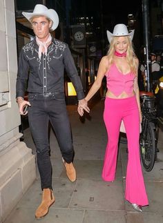 a man and woman in cowboy hats are walking down the street holding hands with each other