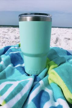 a green cup sitting on top of a blue and white towel next to the ocean