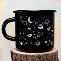 a black coffee mug with space drawings on it sitting on top of a tree stump