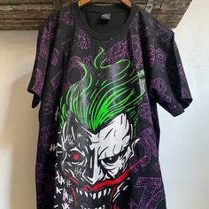 a t - shirt with the joker on it hanging from a wooden hanger in front of a white wall