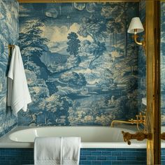 a bathroom with blue and white wallpaper, gold faucet, and bathtub