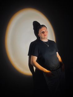 a man standing in front of a black background with an orange circle around him and his head tilted to the side