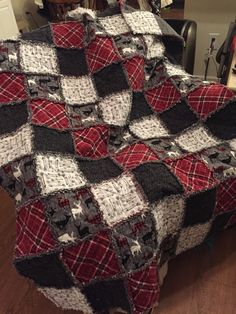 a red, black and white quilt sitting on top of a wooden floor next to a chair