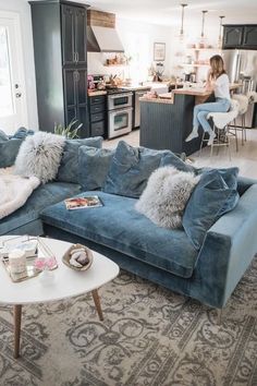 a living room filled with furniture and a woman sitting at a kitchen counter in the background