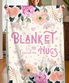 a woman holding up a blanket that says blanket hugs with pink flowers and leaves on it