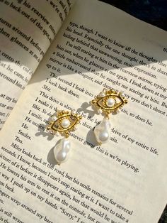 the book is open and has two pearls hanging from it's sides, along with a pair of gold - plated earrings