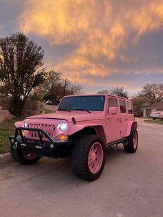 a pink jeep parked on the side of a road in front of a house at sunset