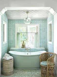 a bath tub sitting under a window next to a chair in a room with blue tiles on the walls