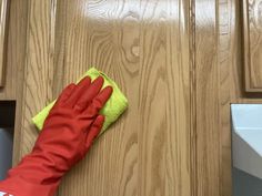 a person wearing red and yellow gloves is cleaning the kitchen cabinets with a micro cloth