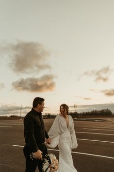 a bride and groom walking in an empty parking lot at sunset with the sun setting behind them