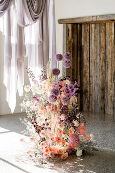 a vase filled with lots of flowers sitting on top of a floor next to a window