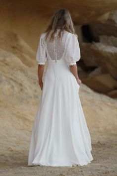 a woman in a white dress is standing on the beach with her back to the camera