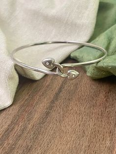 This Interlinking Love Hearts Silver Bangle, a symbol of love and connection beautifully expressed in sterling silver. This bangle is a charming and meaningful accessory that captures the essence of heartfelt relationships. Crafted from high-quality sterling silver, this bangle features a unique design of interlocking love hearts. The hearts are delicately intertwined, representing the unbreakable bonds of love, friendship, and unity. The smooth and polished surface of the silver adds a touch of Anniversary Sterling Silver Bangle With Silver Clasp, Sterling Silver Clasp Bracelet For Valentine's Day Anniversary, Anniversary Bracelet With Sterling Silver Clasp For Valentine's Day, Valentine's Day Anniversary Bracelet With Sterling Silver Clasp, Sterling Silver Double Heart Bracelet, Sterling Silver Heart Bracelet For Friendship, Adjustable Sterling Silver Heart Bangle Bracelet, Sterling Silver Promise Bracelets, Sterling Silver Heart Bracelet For Promise